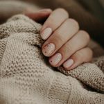Close-up of a hand with polka dot manicured nails wrapped in a knitted sweater.